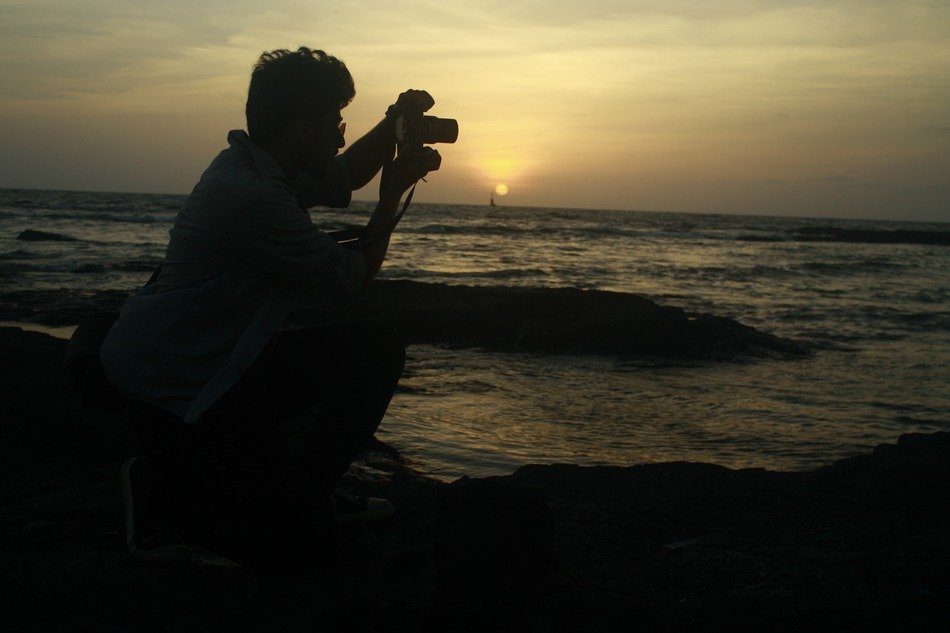 man photographs sunset on the background of water