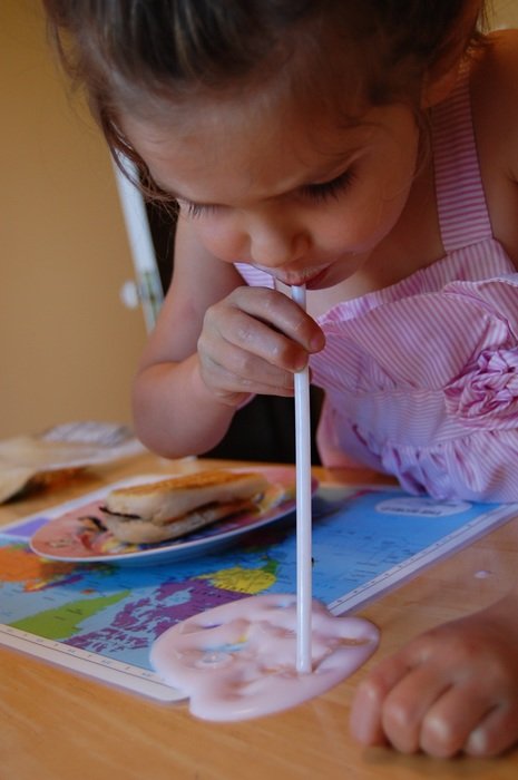 Little girl drinks spilled milk through a straw