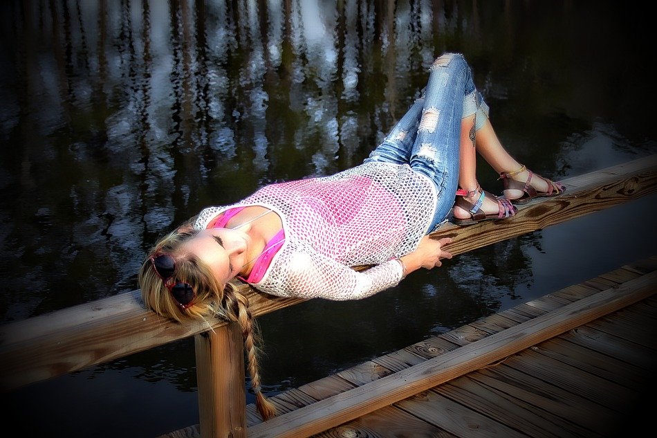 young girl laying down on wooden fence of pier at water