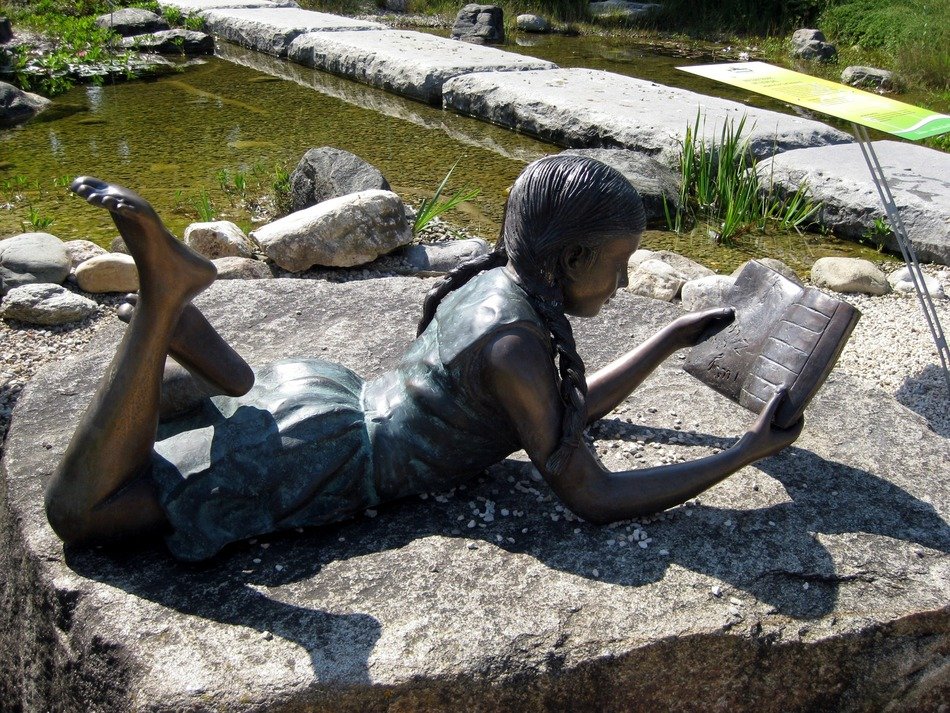 girl read in garden as a park statue
