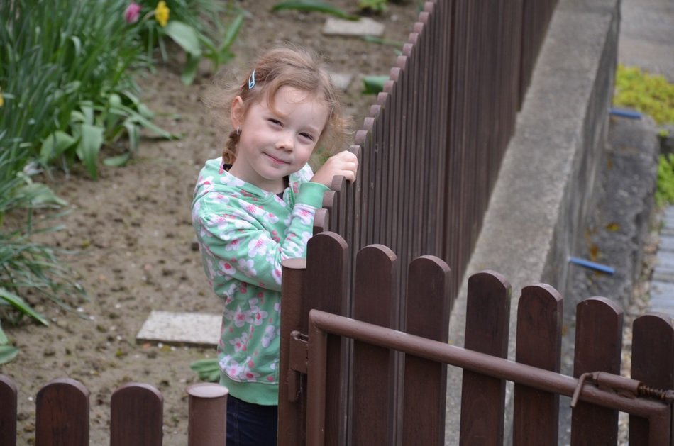 cute girl is standing in the garden, near the wooden fence