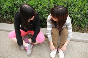 two asian girls sit on pavement near the plants