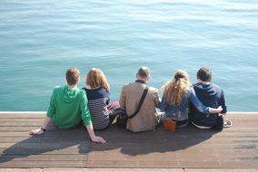 group of people is sitting on a wooden pier