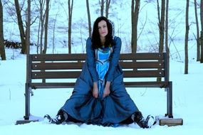 nice girl in a blue princess dress sitting on the snowy bench