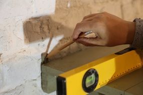 female hand marking wall with pencil over Spirit level