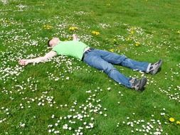 man in a yellow t-shirt is lying on the grass and flowers