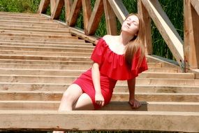 beautiful blonde girl in a red dress sitting on bridge