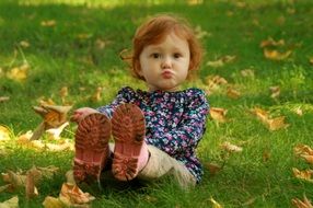 innocent baby girl on a background of green grass with yellow leaves