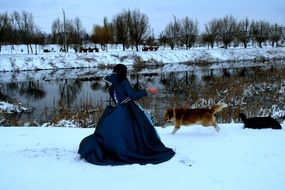 back view of princess in a blue dress on a background of the running dogs through the snow