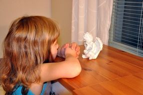 child girl praying at little angel figure