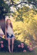 girl near a bush of pink peonies in the sunlight