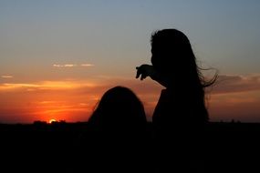 silhouette of a girl pointing to a colorful sunset