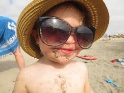 Funny child in sand wearing glasses and sunhat