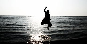 happy boy jumping above water, silhouette