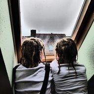 two sisters look out the window in rainy weather