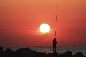 fisherman with a fishing rod against a pink sunset