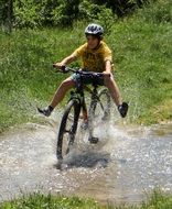 boy riding a bike in a spray of water among nature