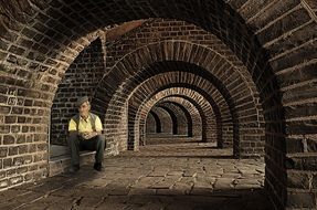 old person sits in a mysterious tunnel of arches