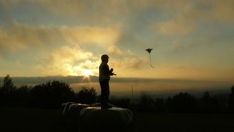 child is flying a kite at sunset