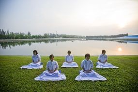 Girls meditate on the green grass near the lake