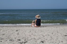 woman and child sitting on sand beach at sea, back view, denmark
