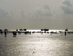 silhouettes of boats and people on the ocean beach