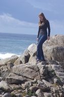 beautiful young girl walking on rocks in front of ocean