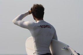 surfer, back view of young man with board at sky