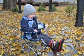 boy sits on a chair in the yard in the fall