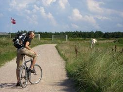 man stands with bike on soil road in countryside, denmark