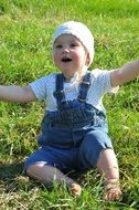 little child in denim overalls on a green meadow