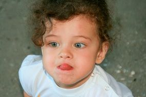 curly-haired, blue-eyed baby showing tongue