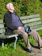 resting old man on the bench among colorful plants