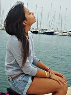 young girl sits in view of sailing boats on water