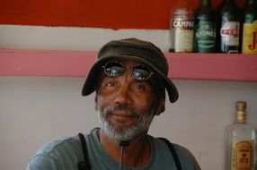 bar owner, old dark skin man with grey beard at shelves with bottles