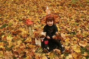 child dressed in carnival witch costume for Halloween on the background of autumn leaves