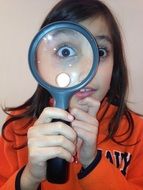 child girl holds loupe in front of eye