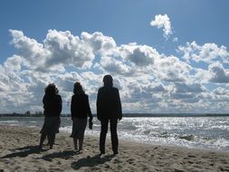 three people on the beach admiring the clouds