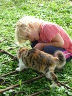 Small blonde girl and beautiful colorful cat on the gras
