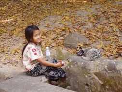 girl sitting on a stone near an animal in cambodia