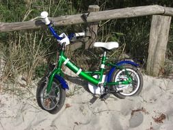 child’s bike on sand at fence