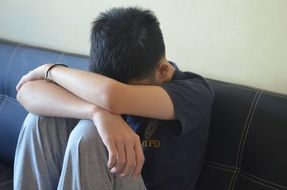 teenager sitting alone on the couch in sadness