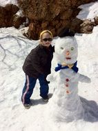 child near a snowman on a sunny day