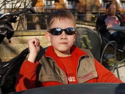 A boy in sunglasses sits on a chair at the table