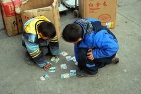 two boys playing trading cards on street