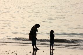 mother and child daughter stay on beach at water