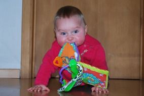 baby girl crawling with a toy in his mouth