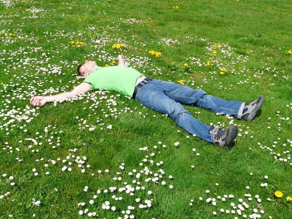 man in a yellow t-shirt is lying on the grass and flowers