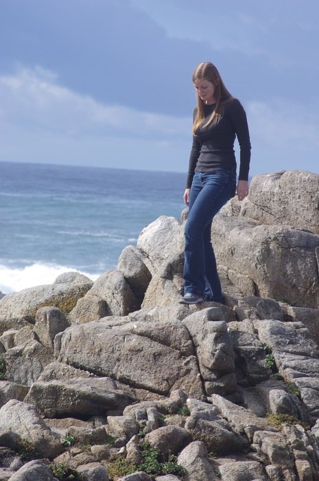 beautiful young girl walking on rocks in front of ocean