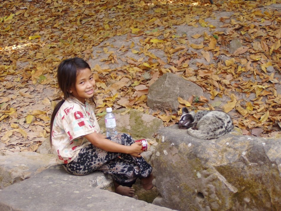girl sitting on a stone near an animal in cambodia